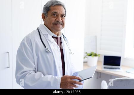 Portrait of smiling senior biracial male doctor using tablet computer Stock Photo