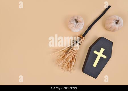 Halloween witch broom, coffin shaped box and velvet pumpkin decorations on beige background Stock Photo