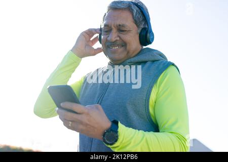 Smiling senior biracial man in sports clothes and headphones using smartphone Stock Photo