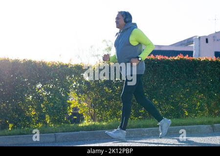 Senior biracial man in sports clothes and headphones jogging in road Stock Photo