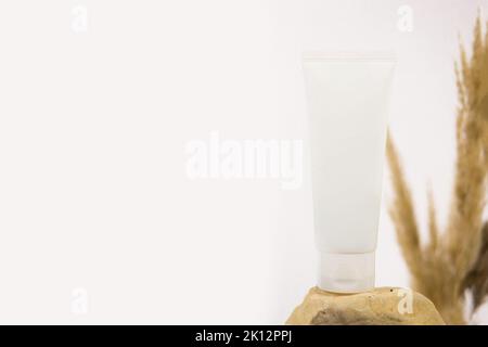 Mockup white squeeze bottle cosmetic tube on stone and pampas grass on white background. Cream, lubricant gel, moisturizer, skincare, sunscreen. Front Stock Photo