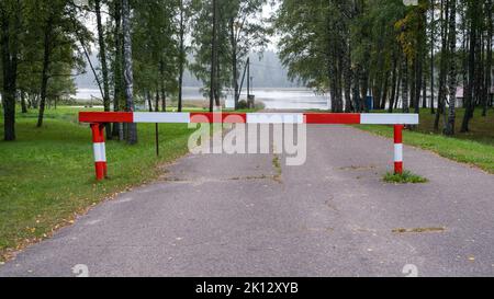 Entry is prohibited. Red and white barrier on the road. The road leads to the lake. Stock Photo