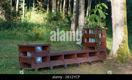 Bench made of windows. Wooden bench in a summer park. Sunny day in the forest on the nature. Wood decor. Trash bin or container near the bench. Stock Photo