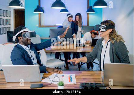 Cheerful multiethnic colleagues gesturing while exploring cyberspace in VR glasses in office Stock Photo