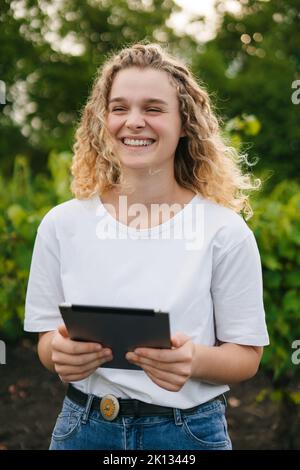 Happy successful woman farmer in vineyard examines and making notes on the tablet. Smart farming and digital agriculture. Smart farming and precision Stock Photo