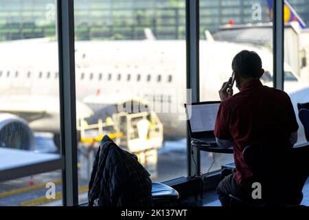 Businessman talking on mobile phone while working on laptop at the airport, Norway, Scandinavia, Europe Stock Photo
