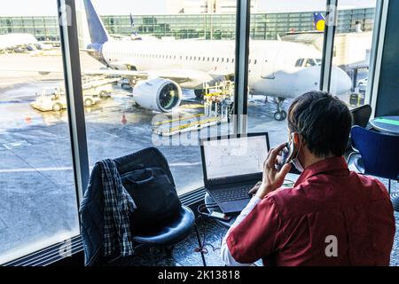 Rear view of mature man using laptop and smartphone while waiting at the airport, Norway, Scandinavia, Europe Stock Photo