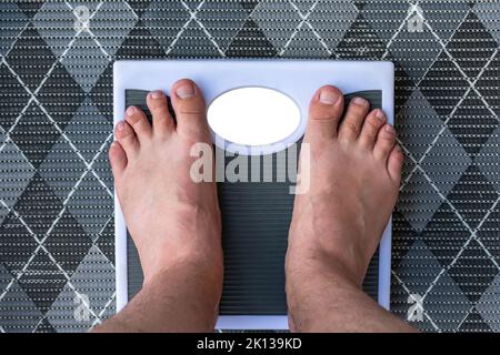 A man measures his weight on floor scales while standing barefoot Stock Photo