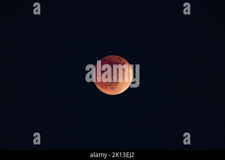 A blood moon total lunar eclipse super moon rising against dark sky Stock Photo