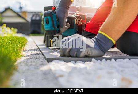 Backyard Garden Turf Grass Installation. Assembling Composite Elements Using Drill Driver Power Tool. Stock Photo