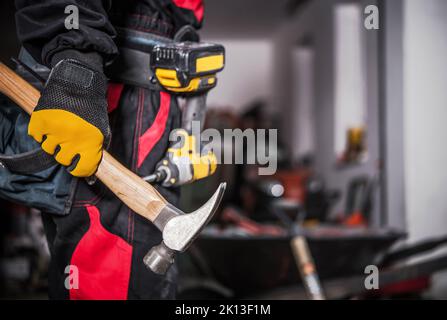 Closeup of Construction Worker Holding a Hammer in His Right Hand. Electric Screwdriver Hanging on a Tool Belt in the Background. Professional Buildin Stock Photo