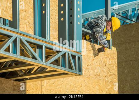 Professional Carpentry Contractor Installing Timber Wood Construction Boards on the Steel Framing Structure of Modern Residential Building Using Elect Stock Photo