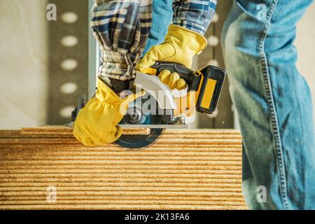 Closeup of Carpenter Cutting Wooden Planks Using Electric Cordless Hand Held Circular Saw. Professional Power Construction Equipment and Tools. Home I Stock Photo