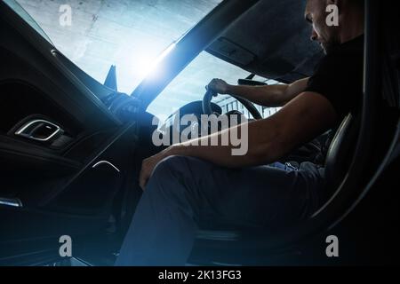 Caucasian Middle Aged Rich Man Sitting on a Driver's Seat in His Super Car Keeping Right Hand on the Steering Wheel and Getting Ready to Leave the Und Stock Photo