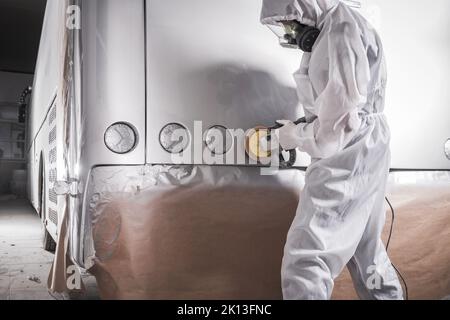 Auto Detailing Workshop Worker in Protective Suit and Mask Polishing Freshly Painted Varnish on a Motor Coach Bus Using Manual Electric Polisher with Stock Photo