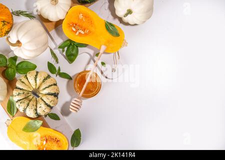 Pumpkins cooking background with various sizes, types and colors squashes with  herbs and spices, olive oil, honey, on white kitchen table background Stock Photo
