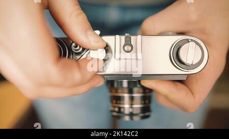 A young photographer changes shutter speed of a vintage old film camera and takes a picture. Stock Photo