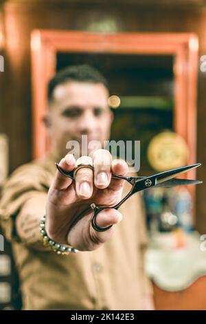 Defocused young barber showing scissors while working in salon Stock Photo