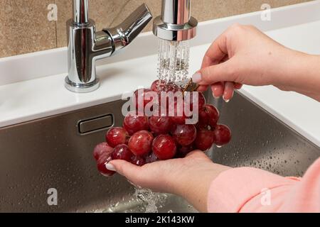 Girl washes red grapes in the kitchen Stock Photo