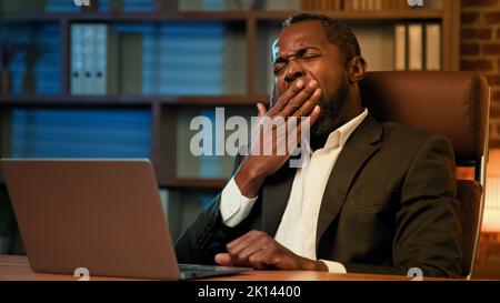 Tired sleepy male manager typing on laptop works in office at night suffering from sleep deprivation feeling fatigue due to overwork drowsy unhappy Stock Photo