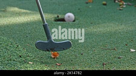 The club just hit the ball during a mini golf game. The ball rolls into the hole Stock Photo