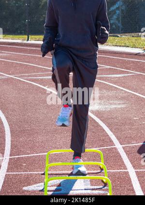 Front view ofr a runner in the A-Position standing over yellow mini banana hurdles on a track. Stock Photo