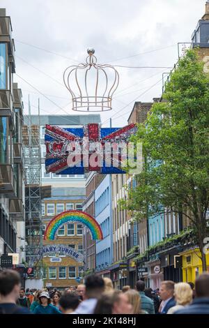 People walk under decorations featuring a crown and a Union flag in central London ahead of the Platinum Jubilee celebrations. Stock Photo