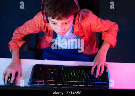 focus on kid, Top view shot of teenager kid with headphones playing video game on computer by using keyboard at home - concept of entertainment Stock Photo