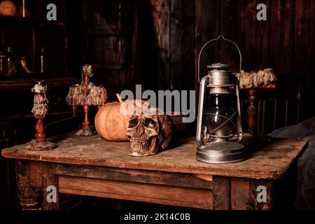 On a wooden table lies a human skull, a pumpkin and a lamp. Halloween Party Stock Photo