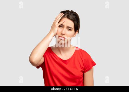 Exhausted woman portrait. Headache frustration. Tired lady holding head by hand. Looking at camera isolated on neutral copy space. Feeling despair. Di Stock Photo
