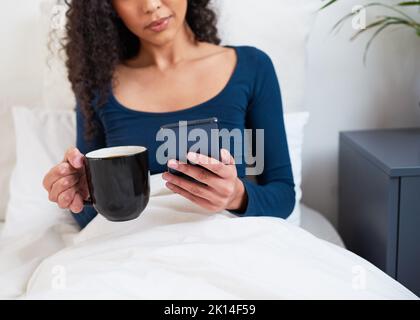 Close up of a woman on cellphone in bed while drinking black coffee Stock Photo