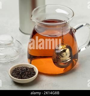 Glass teapot with a metal tea infuser and bowl with German Ostfriesen tea in front Stock Photo