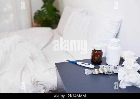 An empty bed with bedside table filled with treatments for flu - pills, tissues Stock Photo