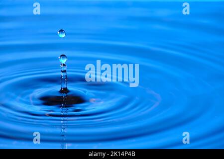 Splash drop of water with diverging water circles, on blue background Stock Photo