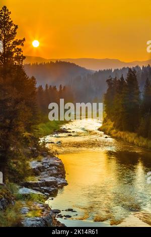 setting sun in a smoky sky over the blackfoot river in the johnsrud recreation area near potomac, montana Stock Photo
