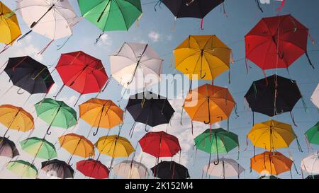 Multicolored umbrellas on the street against the sky swinging in the wind. Stock Photo