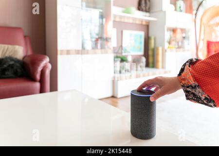 A smart speaker assistant stands in a bright living room. A female hand presses a button. Copy space. Stock Photo