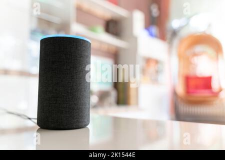 A smart speaker assistant stands in a bright living room. A light blue circle lights up at the top, the device is on reception. Lots of copy space. Stock Photo