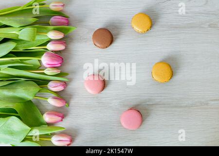 Tulips with pink flowers in front of white wood. Colorful delicious macarons in front of white wood. Top view photographed from above. Stock Photo