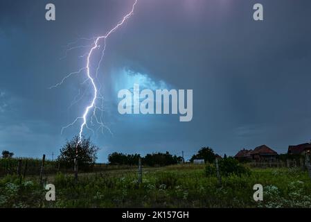 Powerful branched thunderbolt of lightning strikes down in an idyllic countryside Stock Photo