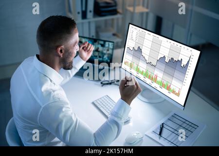 Successful Stock Market Trader Looking At Graphs On Multiple Screens In Office Stock Photo