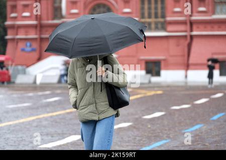 Rain in city, slim girl in jeans and jacket walk with black umbrella on a street. Rainy weather in autumn Stock Photo