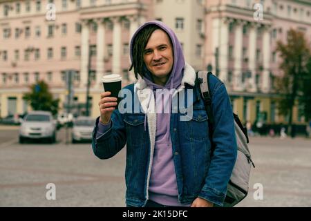 Hipster man with dreadlocks drinking hot coffee on street. Young male in warm clothes drinking hot beverage. Stock Photo