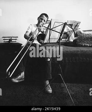 Undated historical image of a boy learning to play trombone in his bedroom. Stock Photo