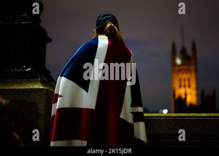 A woman draped in a Union Flag stands in the queue on the South Bank in London opposite the Palace of Westminster, as they wait to view Queen Elizabeth II lying in state ahead of her funeral on Monday. Picture date: Thursday September 15, 2022. Stock Photo