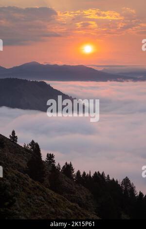 The sun rising through forest fire smoke above a foggy morning below Signal Mountain. Grand Teton National Park, Wyoming Stock Photo