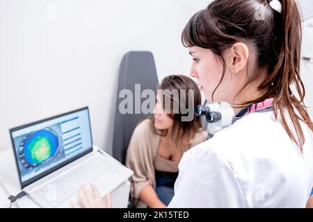 From above of focused female ophthalmologist using laptop with eyesight check up results during appointment with patient in modern hospital Stock Photo