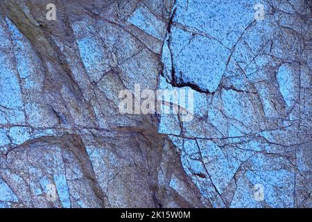Textured background of natural granite rock cliff covered with uneven cracks in evening Stock Photo