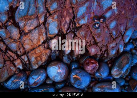 From above of small colorful smooth pebbles placed on hole in metamorphic stone with wavy abstract ornament in nature Stock Photo