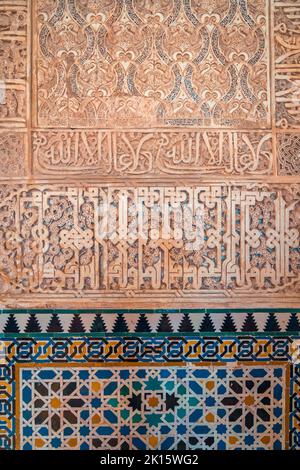 Colorful mosaic tiles forming geometric ornament under Arabic inscription on wall of aged palace of Alhambra fortress complex in Granada, Spain Stock Photo